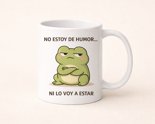 taza blanca con frase “No estoy de humor ni lo voy a estar” y rana kawaii, ambiente cálido con café y detalles beige